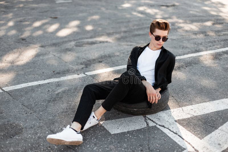 Hombre Elegante Joven Del Inconformista Con El Peinado De Moda En Una Camisa Negra Elegante Pantalones Rayados En Sentarse Bla Imagen de archivo - Imagen de camino, individuo: 154111535