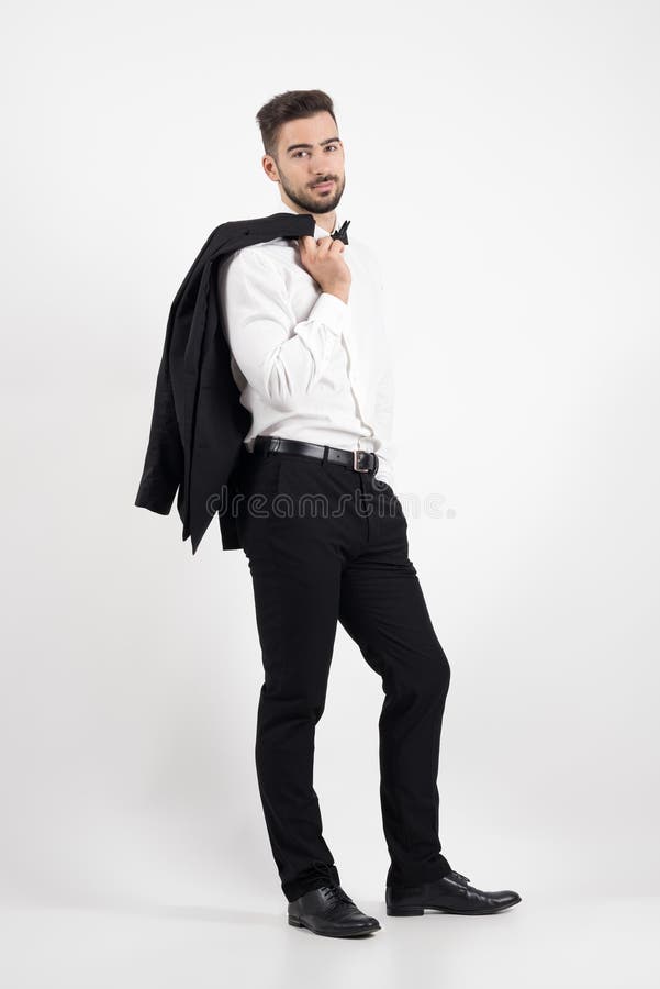 Hombre elegante que sostiene la capa del smoking sobre su hombro que mira la cámara foto de archivo libre de regalías Hombre elegante que sostiene la capa del smoking sobre su hombro que mira la cámara foto de archivo libre de regalías