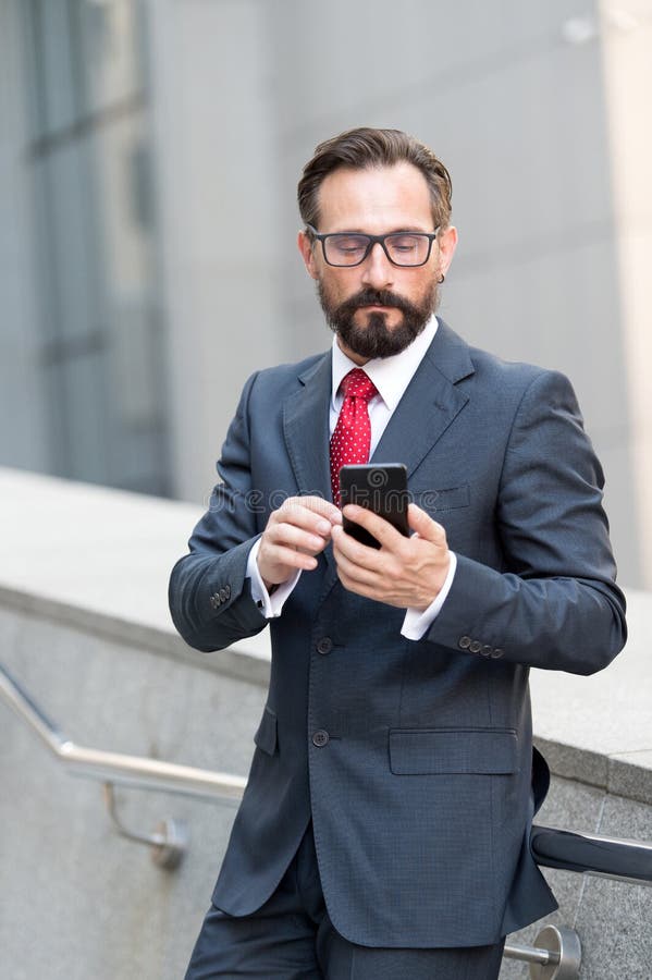 Hombre elegante tranquilo que mira la pantalla de su smartphone mientras que siendo solo imagen de archivo libre de regalías Hombre elegante tranquilo que mira la pantalla de su smartphone mientras que siendo solo imagen de archivo libre de regalías