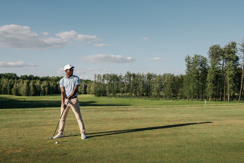 Hombre en el casquillo que detiene al club de golf y que golpea la bola en césped verde imágenes de archivo libres de regalías Hombre en el casquillo que detiene al club de golf y que golpea la bola en césped verde imágenes de archivo libres de regalías