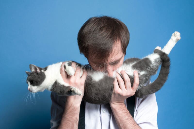 hombre en gato gris del estómago y blanco lindo que se sostiene y que se besa de la camisa y de la liga negra fotografía de archivo libre de regalías hombre en gato gris del estómago y blanco lindo que se sostiene y que se besa de la camisa y de la liga negra fotografía de archivo libre de regalías