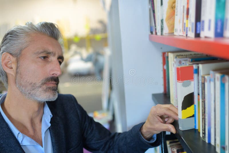 Hombre en la biblioteca que elige los libros imágenes de archivo libres de regalías Hombre en la biblioteca que elige los libros imágenes de archivo libres de regalías