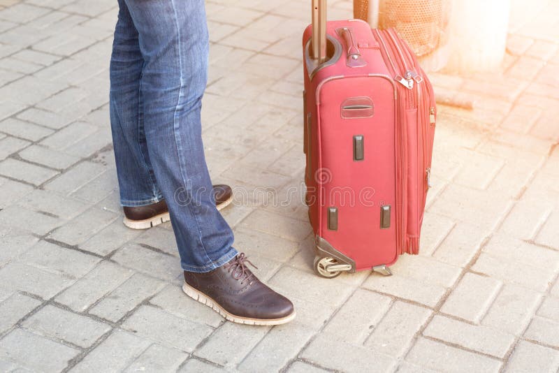 Hombre en la ropa casual que se coloca con la maleta roja en la estación Viaje dealyed que espera del viajero moderno joven para fotografía de archivo libre de regalías Hombre en la ropa casual que se coloca con la maleta roja en la estación Viaje dealyed que espera del viajero moderno joven para fotografía de archivo libre de regalías