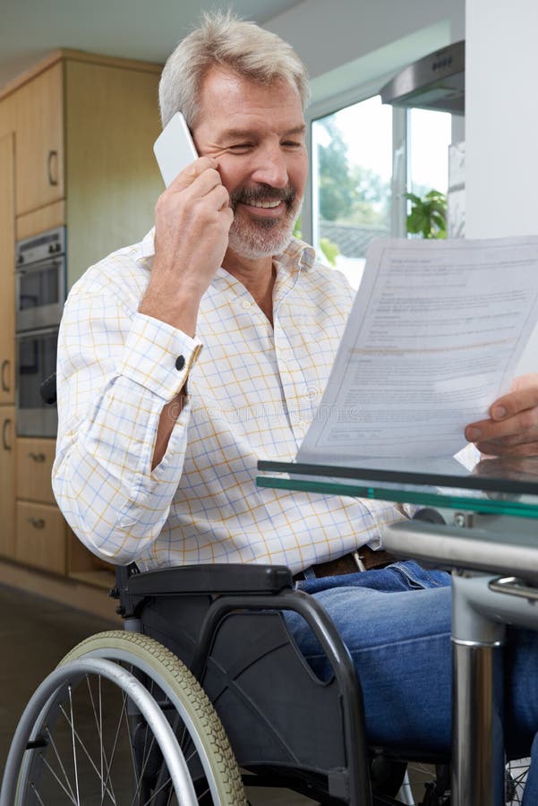 Hombre en la silla de ruedas que hace llamada de teléfono mientras que lee la letra fotos de archivo Hombre en la silla de ruedas que hace llamada de teléfono mientras que lee la letra fotos de archivo