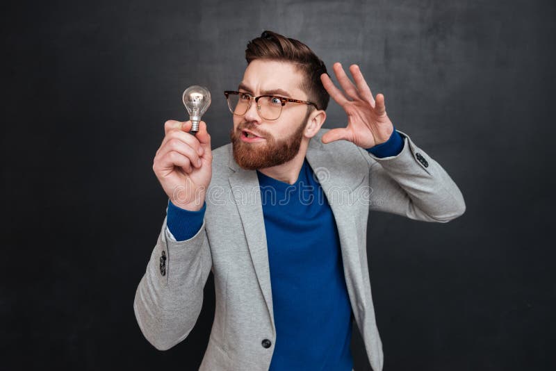 Hombre en las lentes que sostienen la bombilla y que gesticulan con la mano imágenes de archivo libres de regalías Hombre en las lentes que sostienen la bombilla y que gesticulan con la mano imágenes de archivo libres de regalías