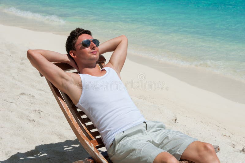 Hombre En Silla Que Toma El Sol En La Playa Imagen de archivo - Imagen