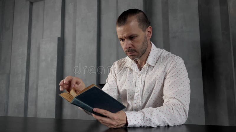 Hombre en una habitación oscura y moderna está leyendo un viejo libro vintage.