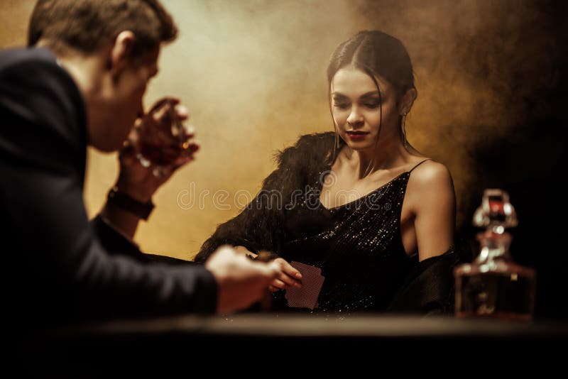 Hombre en whisky de consumición del traje mientras que juega el póker con la mujer hermosa fotografía de archivo Hombre en whisky de consumición del traje mientras que juega el póker con la mujer hermosa fotografía de archivo