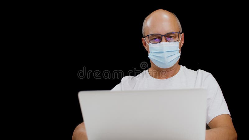 Hombre enfocado en mascarillas médicas y anteojos trabajando con laptop