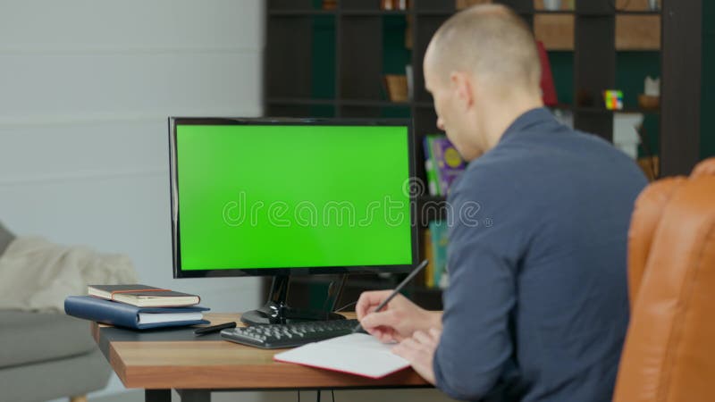 Hombre escribiendo en un portátil con lápiz cerca de una computadora con pantalla verde maquillada almacen de video