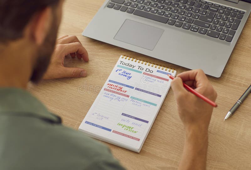 Hombre escribiendo una lista de tareas para hoy en su cuaderno de espiral mientras trabaja en su oficina principal. foto de archivo libre de regalías