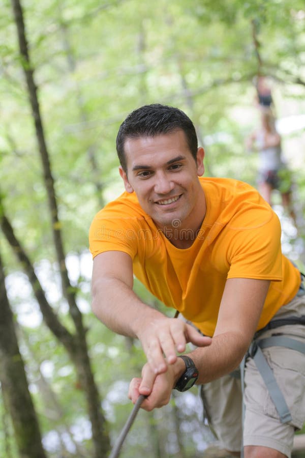 Hombre feliz en el parque extremo de la cuerda con mosquetones foto de archivo Hombre feliz en el parque extremo de la cuerda con mosquetones foto de archivo