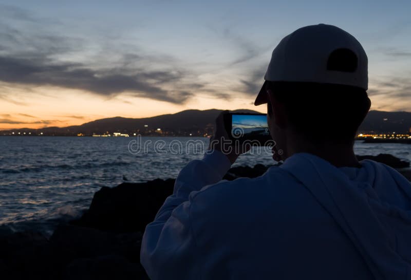 Hombre fotografiando una puesta de sol con su smartphone imágenes de archivo libres de regalías