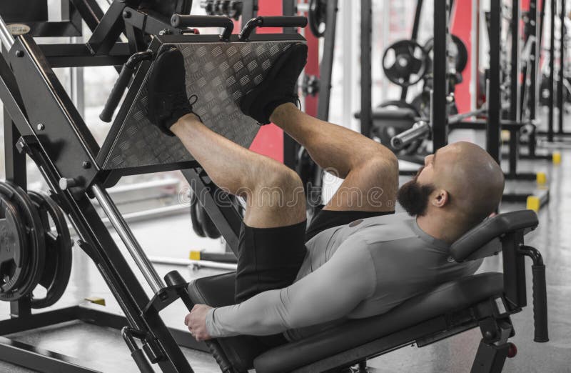 Hombre fuerte con el cuerpo muscular del ajuste que hace los ejercicios en la máquina de la prensa de la pierna, entrenamiento imágenes de archivo libres de regalías Hombre fuerte con el cuerpo muscular del ajuste que hace los ejercicios en la máquina de la prensa de la pierna, entrenamiento imágenes de archivo libres de regalías