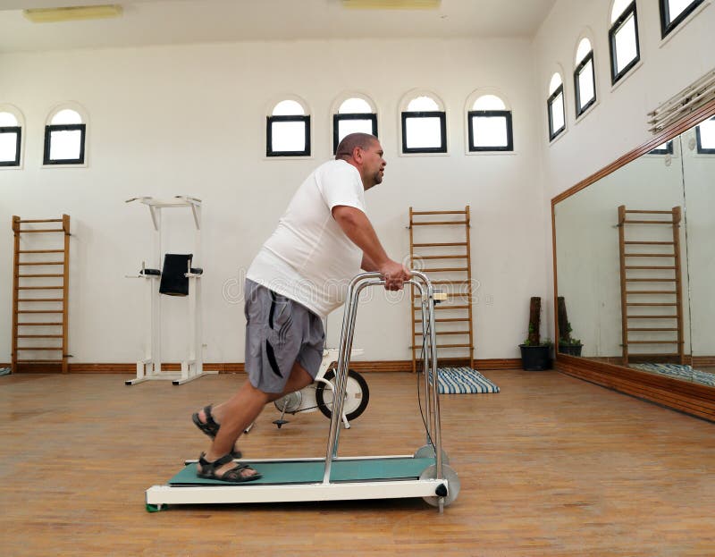 Hombre gordo que corre en la rueda de ardilla del instructor imagen de archivo Hombre gordo que corre en la rueda de ardilla del instructor imagen de archivo