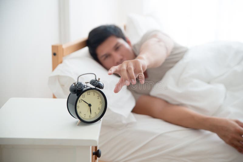 Hombre hermoso asiático despertado por el despertador en la cama en el tiempo de mañana foto de archivo Hombre hermoso asiático despertado por el despertador en la cama en el tiempo de mañana foto de archivo