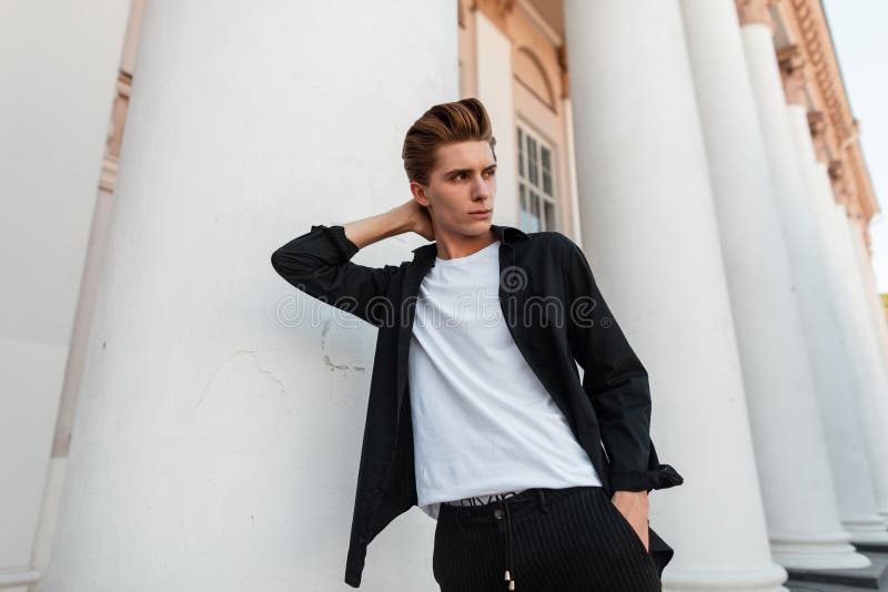 Hombre hermoso joven de moda con el peinado elegante en la ropa elegante que presenta cerca de un edificio del vintage con las co fotos de archivo libres de regalías Hombre hermoso joven de moda con el peinado elegante en la ropa elegante que presenta cerca de un edificio del vintage con las co fotos de archivo libres de regalías