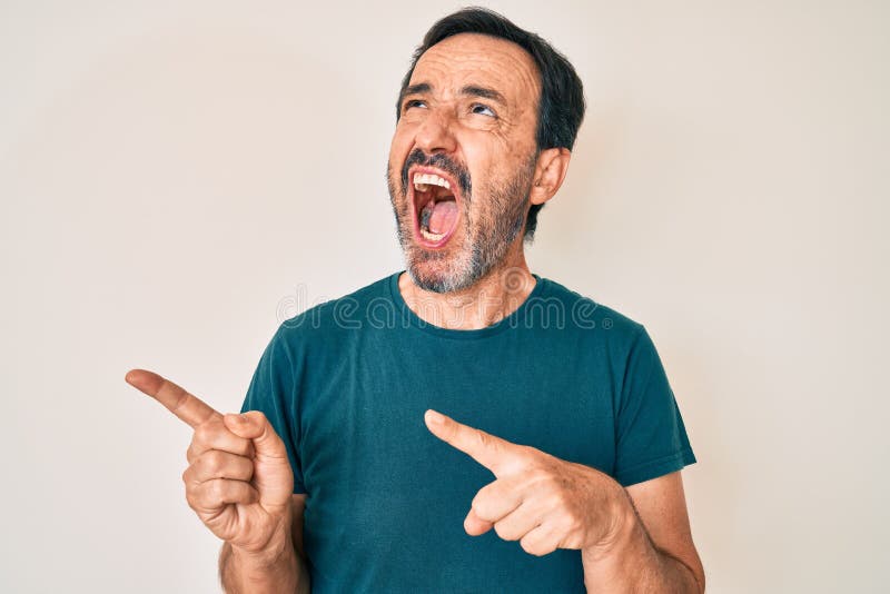Hombre hispano de mediana edad señalando con los dedos hacia el lado enojado y loco gritando frustrado y furioso gritando con ira fotografía de archivo