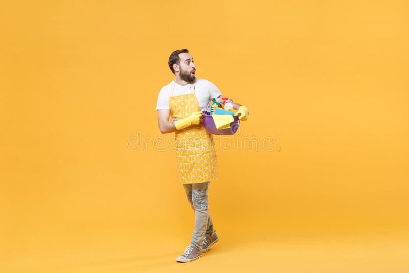 Hombre impactado esposo de la casa en guantes de goma de delantal sostiene botellas detergentes lavadoras de cuencas haciendo tare foto de archivo