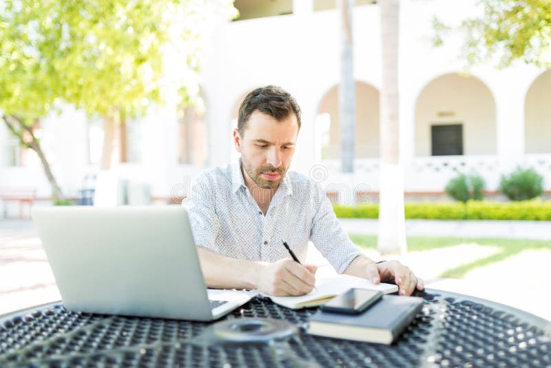 Self-employed man with laptop and books preparing schedule at table in garden. Self-employed man with laptop and books preparing schedule at table in garden