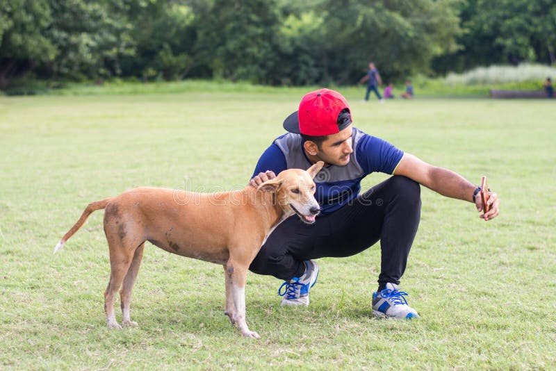 Hombre indio joven del atleta que juega con el perro y que toma selfies en tierra de deportes mientras que activa Deportes y conc