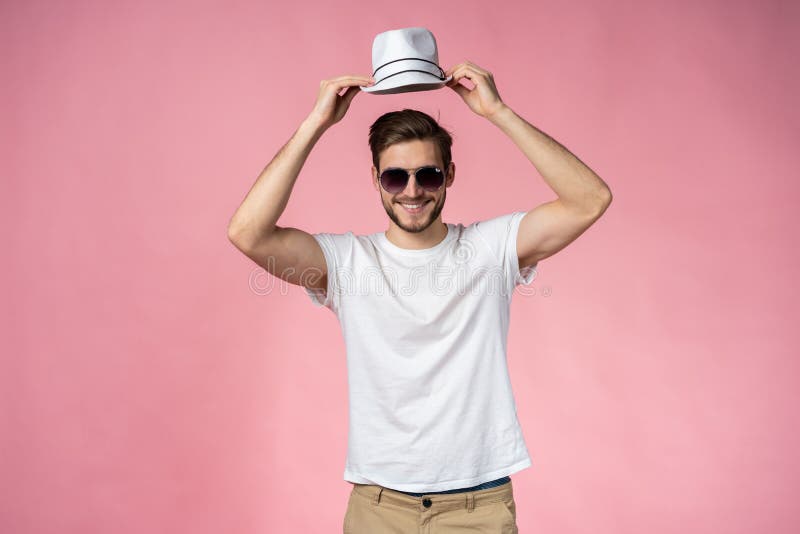 Hombre joven alegre en el sombrero y las gafas de sol que se colocan y que sonríen sobre fondo rosado foto de archivo libre de regalías Hombre joven alegre en el sombrero y las gafas de sol que se colocan y que sonríen sobre fondo rosado foto de archivo libre de regalías