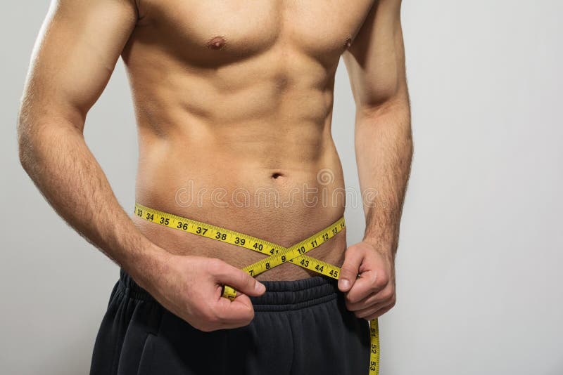 Hombre joven apto que mide su cintura muscular imágenes de archivo libres de regalías Hombre joven apto que mide su cintura muscular imágenes de archivo libres de regalías