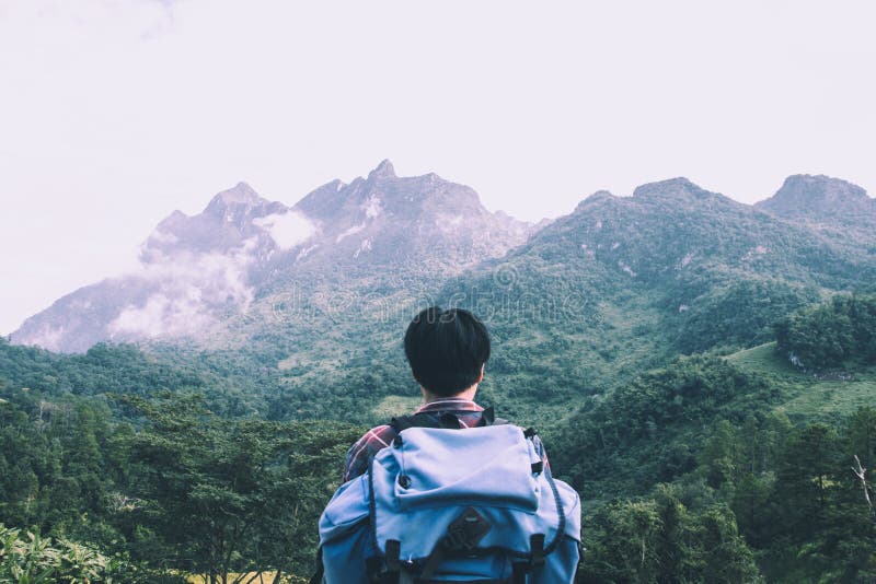 Hombre joven asiático en camisa escocesa y el sombrero negro que caminan en el pico de montaña sobre las nubes y el caminante de foto de archivo libre de regalías Hombre joven asiático en camisa escocesa y el sombrero negro que caminan en el pico de montaña sobre las nubes y el caminante de foto de archivo libre de regalías