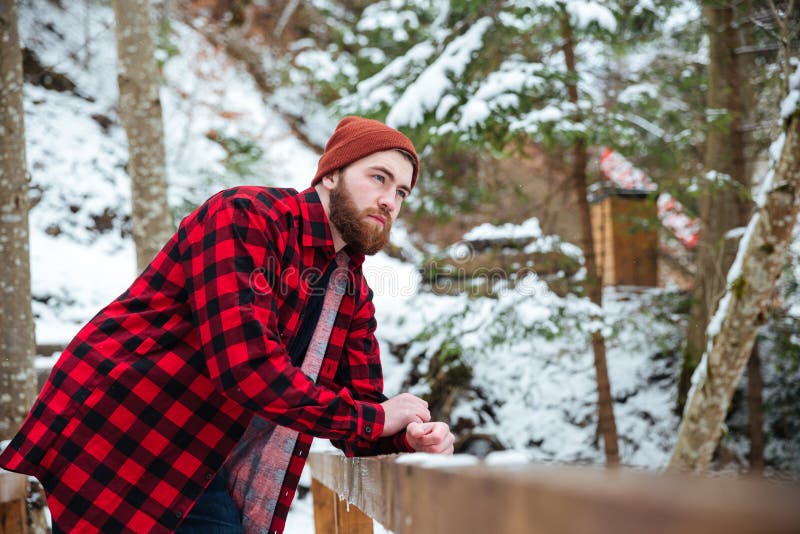 Hombre joven barbudo pensativo que se coloca en bosque del invierno fotos de archivo libres de regalías Hombre joven barbudo pensativo que se coloca en bosque del invierno fotos de archivo libres de regalías