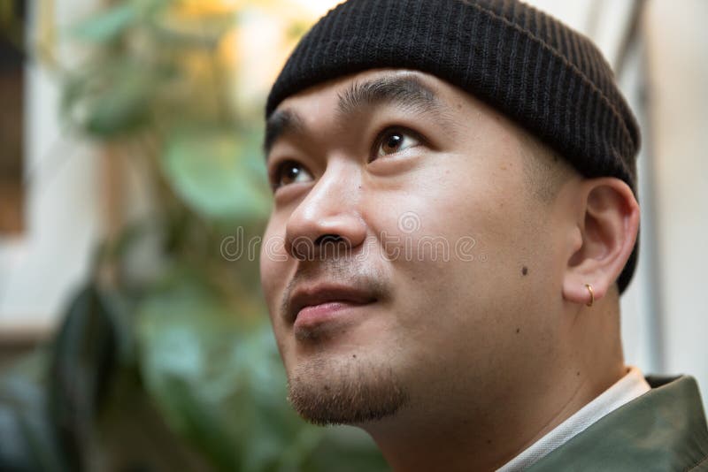 Hombre joven chino con el pendiente contra fondo de la planta verde imágenes de archivo libres de regalías Hombre joven chino con el pendiente contra fondo de la planta verde imágenes de archivo libres de regalías