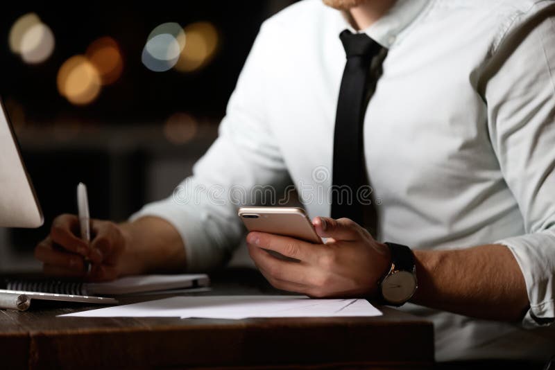 Hombre joven con el teléfono móvil que trabaja en oficina en la noche foto de archivo libre de regalías Hombre joven con el teléfono móvil que trabaja en oficina en la noche foto de archivo libre de regalías