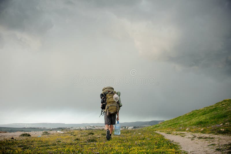 Hombre joven de la vista posterior que camina con una mochila que camina en la costa imagen de archivo libre de regalías Hombre joven de la vista posterior que camina con una mochila que camina en la costa imagen de archivo libre de regalías