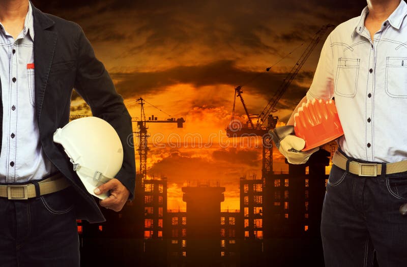Hombre joven del ingeniero que se opone con el casco de seguridad al edificio foto de archivo Hombre joven del ingeniero que se opone con el casco de seguridad al edificio foto de archivo