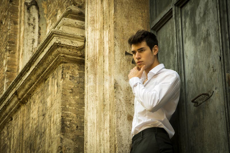 Hombre joven elegante que se inclina contra la pared vieja y fotografía de archivo Hombre joven elegante que se inclina contra la pared vieja y fotografía de archivo