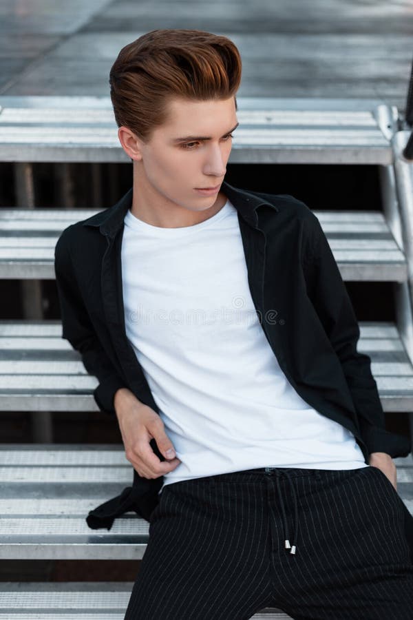 Hombre Joven Elegante Urbano Con Un Peinado De Moda En Una Camisa Negra Clásica En Una Blanca En La Presentación Elegant Imagen de archivo - Imagen de sentada, 154111007