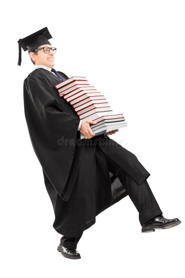 Hombre joven en el manojo que lleva del vestido de la graduación de libros foto de archivo Hombre joven en el manojo que lleva del vestido de la graduación de libros foto de archivo