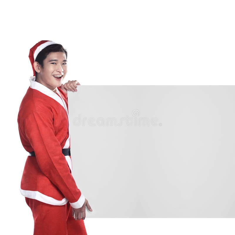 Hombre joven en el traje de Santa Claus detrás del tablero blanco imagen de archivo Hombre joven en el traje de Santa Claus detrás del tablero blanco imagen de archivo