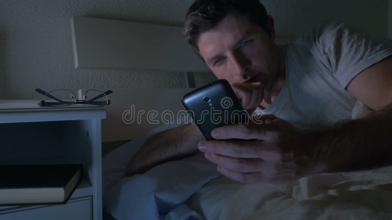 Hombre joven en sofá de la cama en casa tarde en la noche usando el teléfono móvil en la luz corta relajada en tecnología de comu