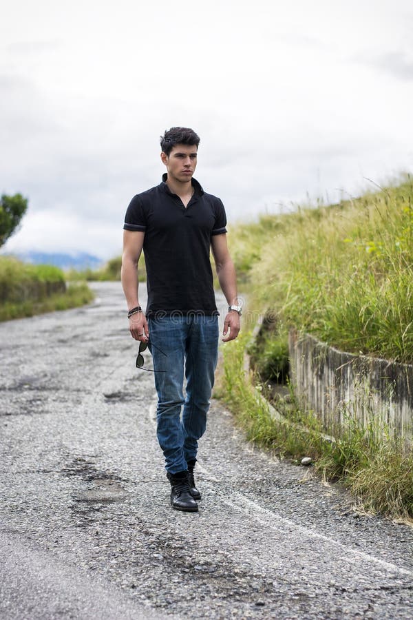 Hombre joven en vaqueros y camiseta negra que camina adelante fotografía de archivo Hombre joven en vaqueros y camiseta negra que camina adelante fotografía de archivo