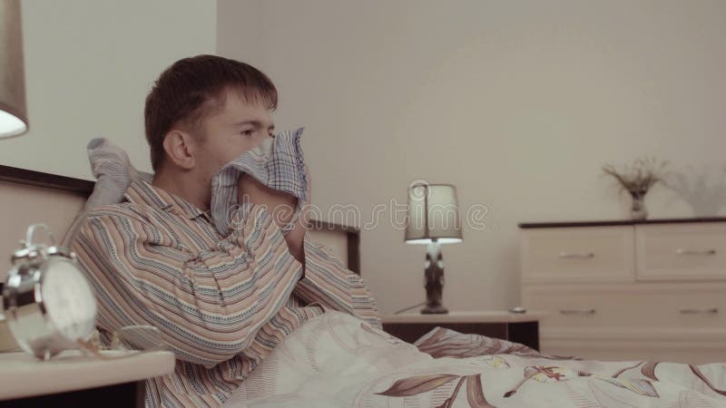 Hombre joven enfermo que miente en cama y que estornuda almacen de video