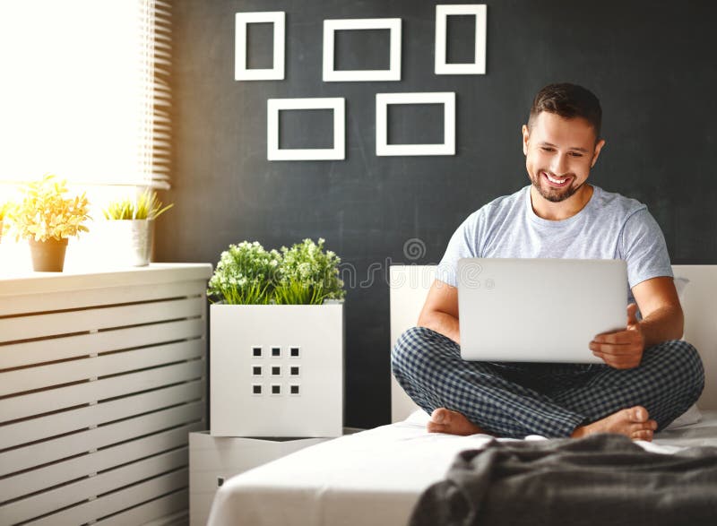 Hombre joven feliz con el ordenador portátil en cama