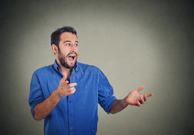Hombre joven feliz que mira para echar a un lado mientras que señala en usted, sorprendido por algo imagenes de archivo Hombre joven feliz que mira para echar a un lado mientras que señala en usted, sorprendido por algo imagenes de archivo