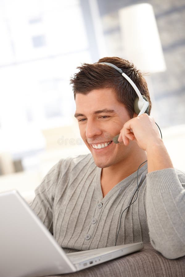 Hombre joven feliz que usa la computadora portátil y el receptor de cabeza imagen de archivo libre de regalías Hombre joven feliz que usa la computadora portátil y el receptor de cabeza imagen de archivo libre de regalías