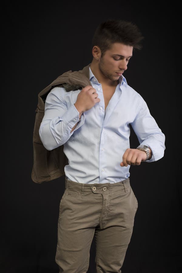 Hombre joven hermoso que comprueba el reloj en su muñeca foto de archivo Hombre joven hermoso que comprueba el reloj en su muñeca foto de archivo