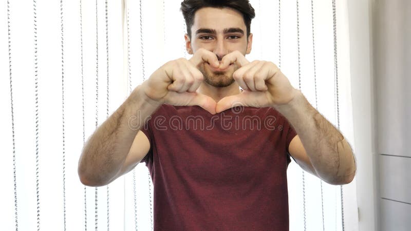 Hombre joven hermoso que hace la muestra del corazón con las manos almacen de video
