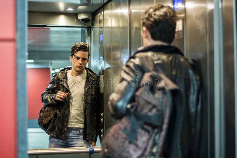 Hombre joven hermoso que se inclina contra el espejo en elevador o la elevación imagenes de archivo Hombre joven hermoso que se inclina contra el espejo en elevador o la elevación imagenes de archivo