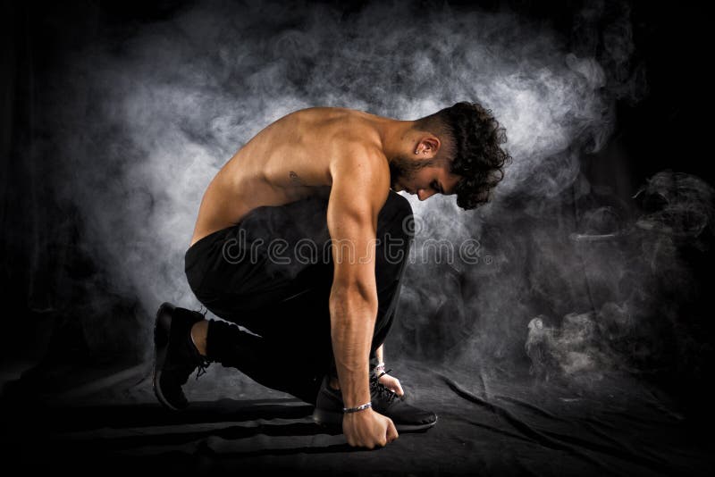 Hombre joven muscular descamisado hermoso que se arrodilla abajo en negro
