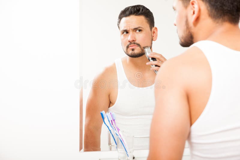 Hombre joven que arregla su barba en el cuarto de baño fotos de archivo Hombre joven que arregla su barba en el cuarto de baño fotos de archivo