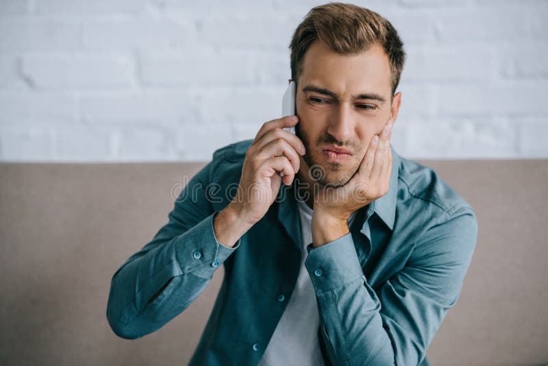 hombre joven que habla por smartphone y que sufre de dolor del mandíbula