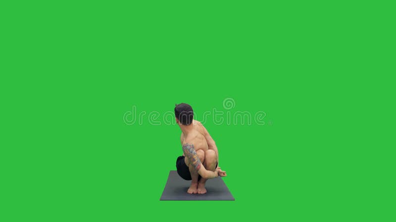 Hombre joven que hace posición en cuclillas con la yoga en una pantalla verde, llave de la torsión y de la curva de la croma